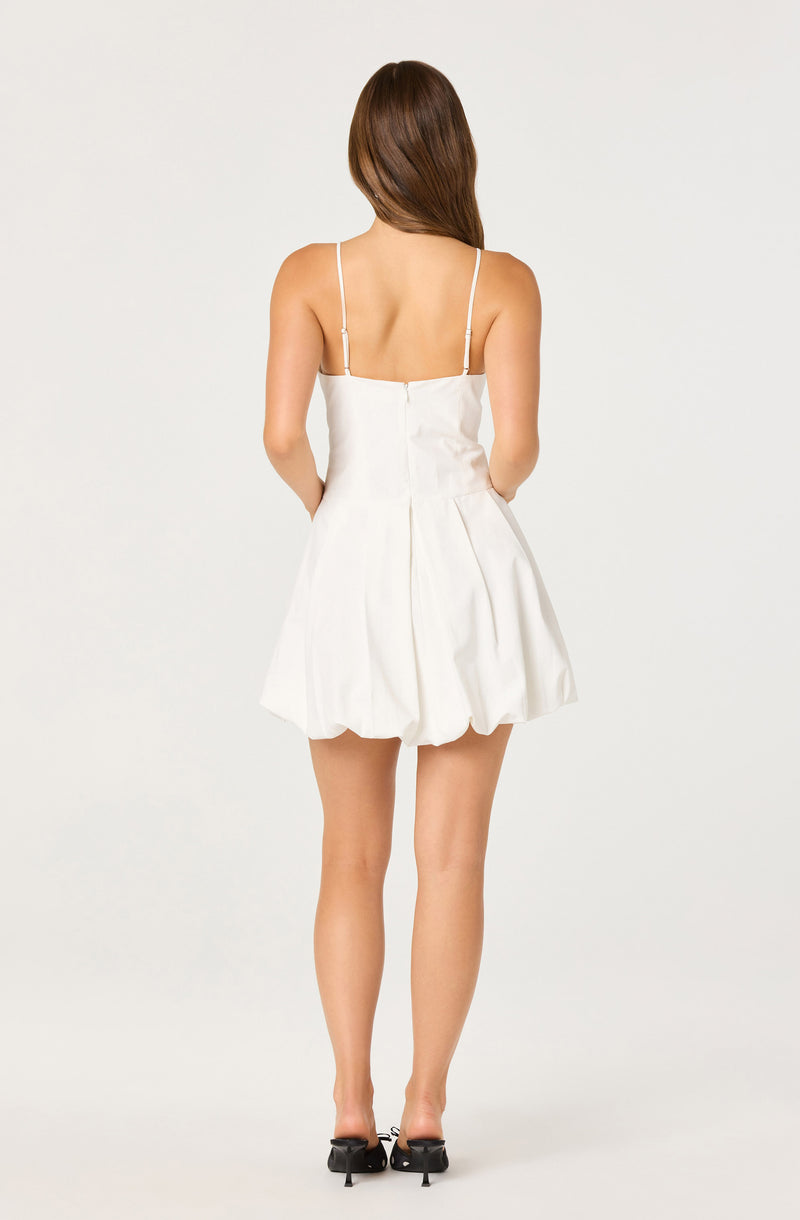 Woman wearing a white sleeveless dress with thin straps and a flared, bubble skirt.