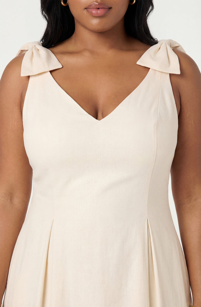 Cream-colored dress with shoulder bows, V-neckline, and pleats at the waist.