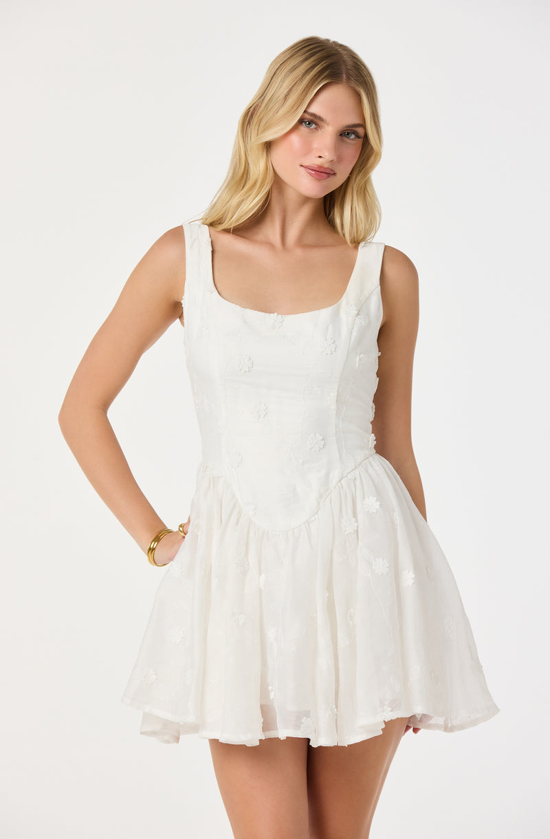 Woman in white sleeveless dress with embroidered floral details and a ruffled skirt.