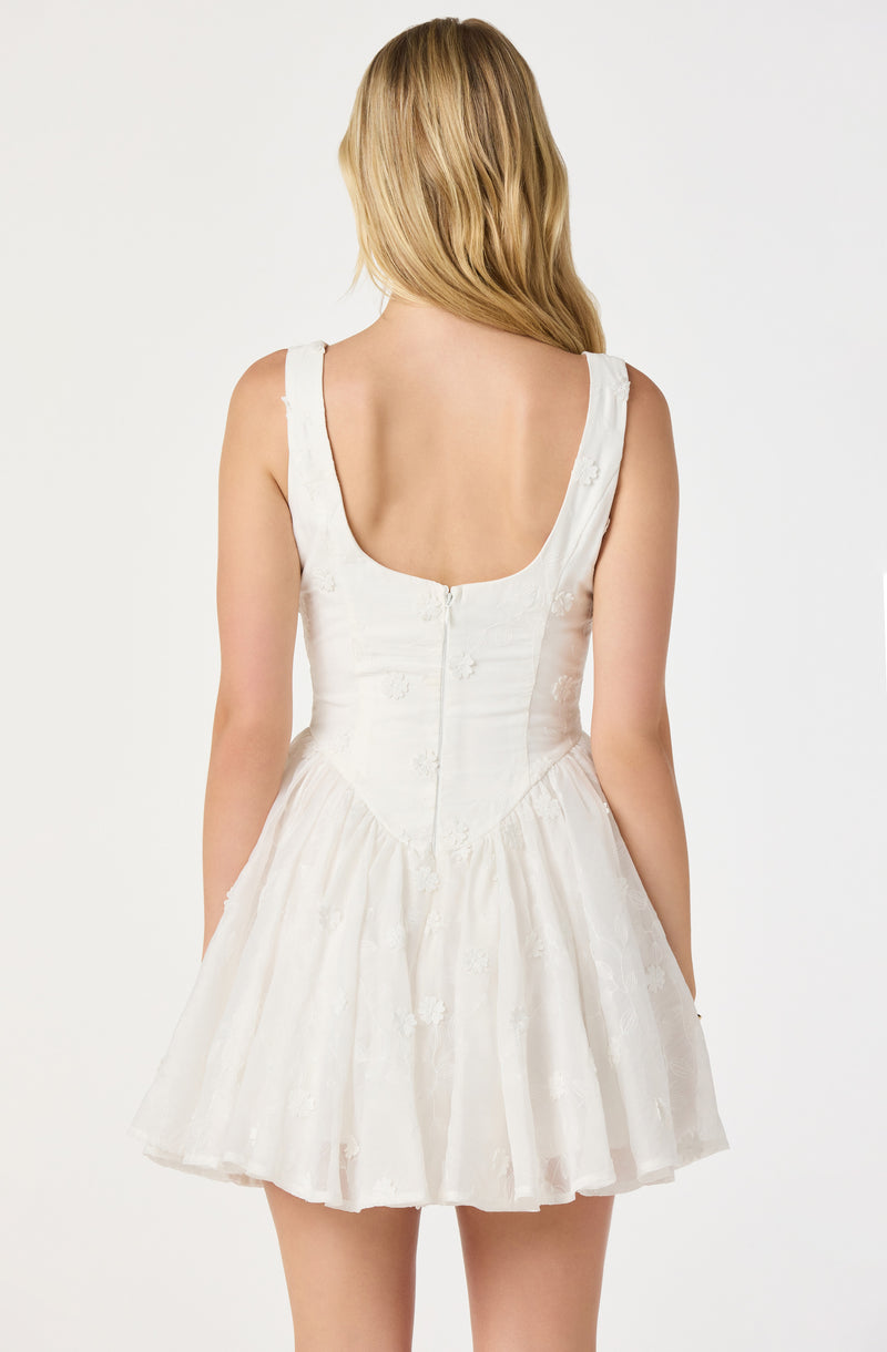 Back view of a woman in a sleeveless white dress with a fitted bodice and a flared, textured skirt.