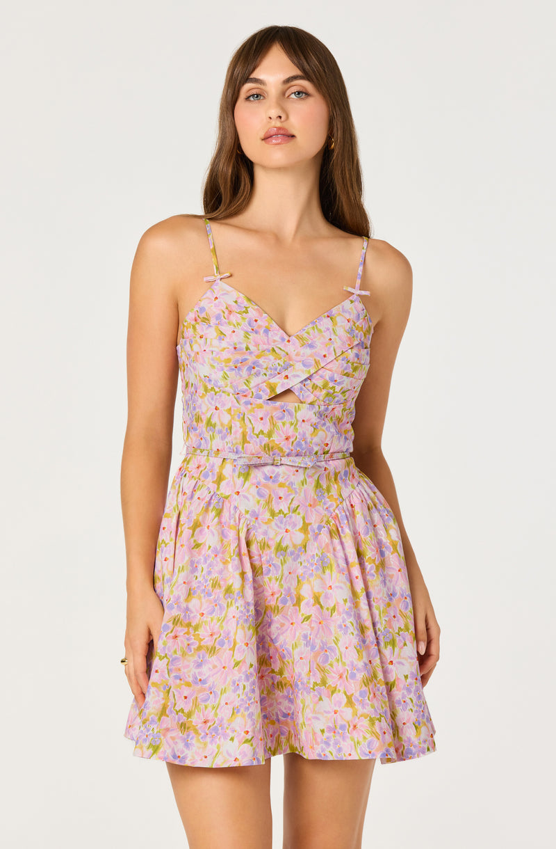 Woman wearing a pastel floral dress with spaghetti straps and a cutout detail at the bust.