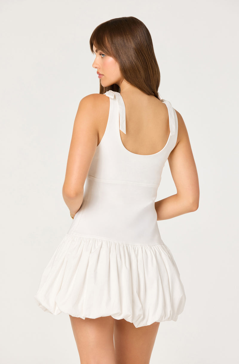 Woman in a sleeveless white dress with tie straps on shoulders and a gathered bubble skirt.