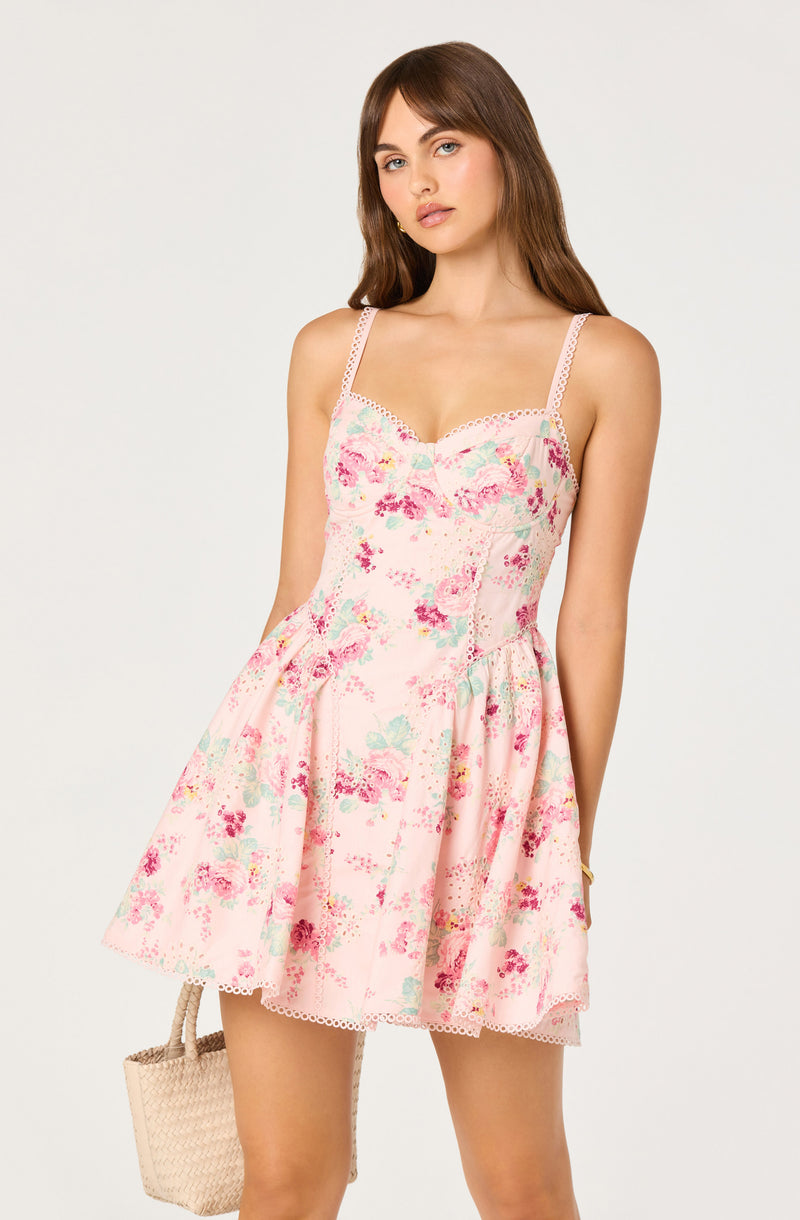 Girl wearing a pink floral dress with thin straps and lace details, holding a woven bag.