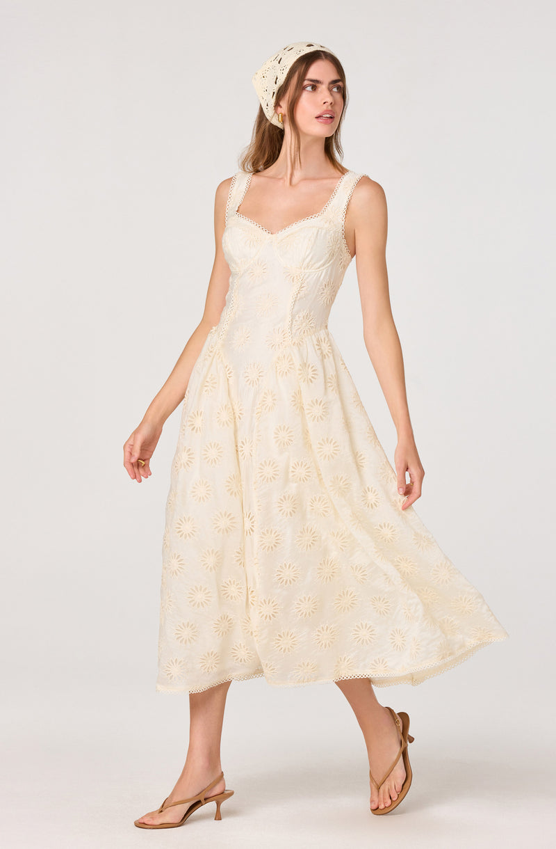 Woman in a cream-colored, sleeveless, embroidered sundress with floral patterns.