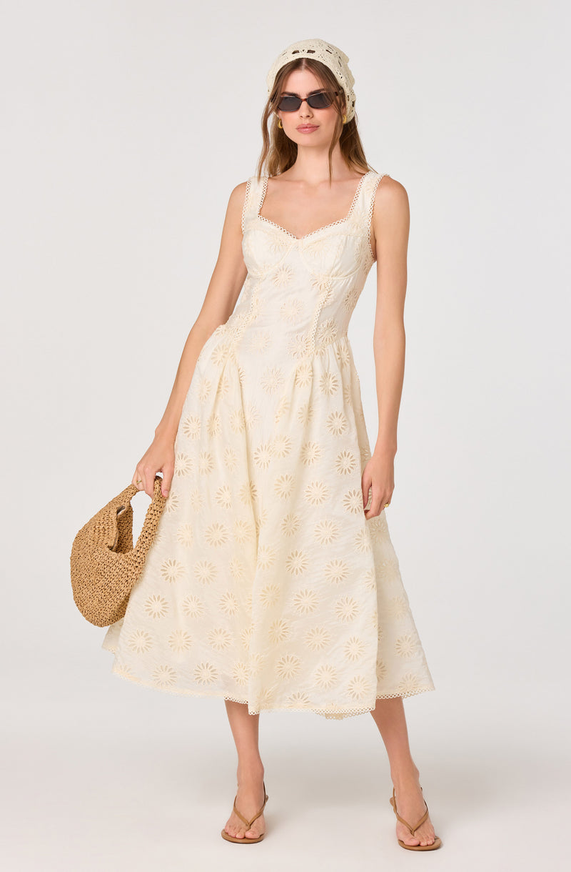 Woman wearing a sleeveless, cream-colored, embroidered dress with a floral pattern.