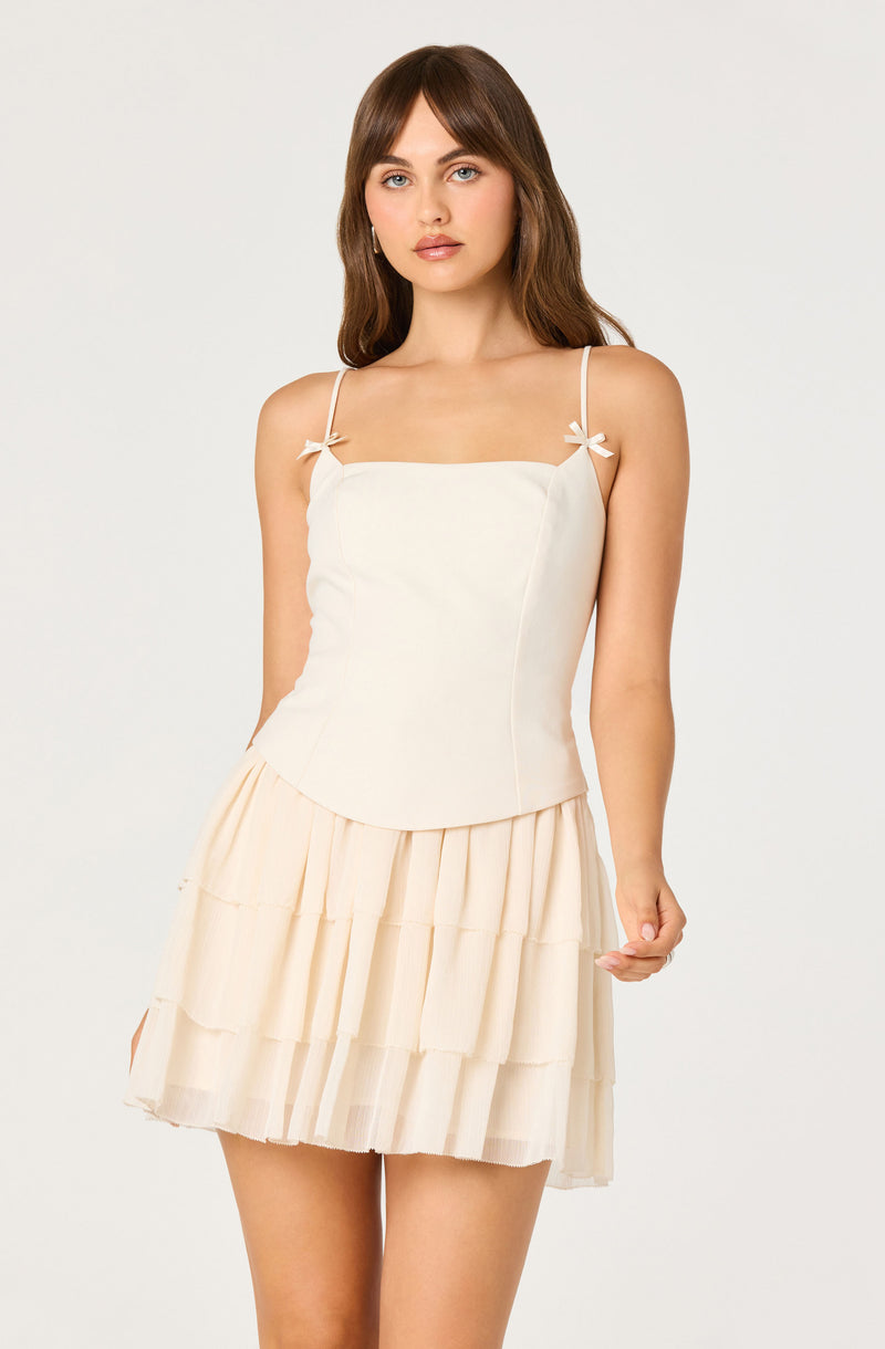 Woman in cream spaghetti strap top with bows and a tiered cream skirt.