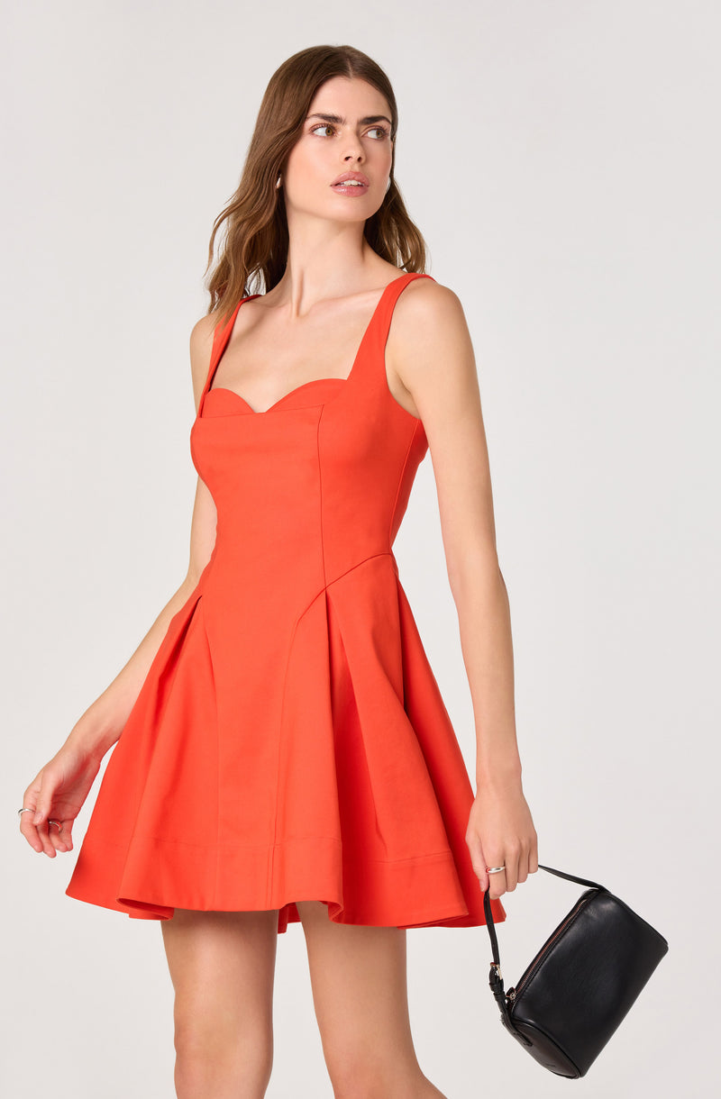 Woman wearing a sleeveless, fitted, orange dress with wide straps and a flared skirt.