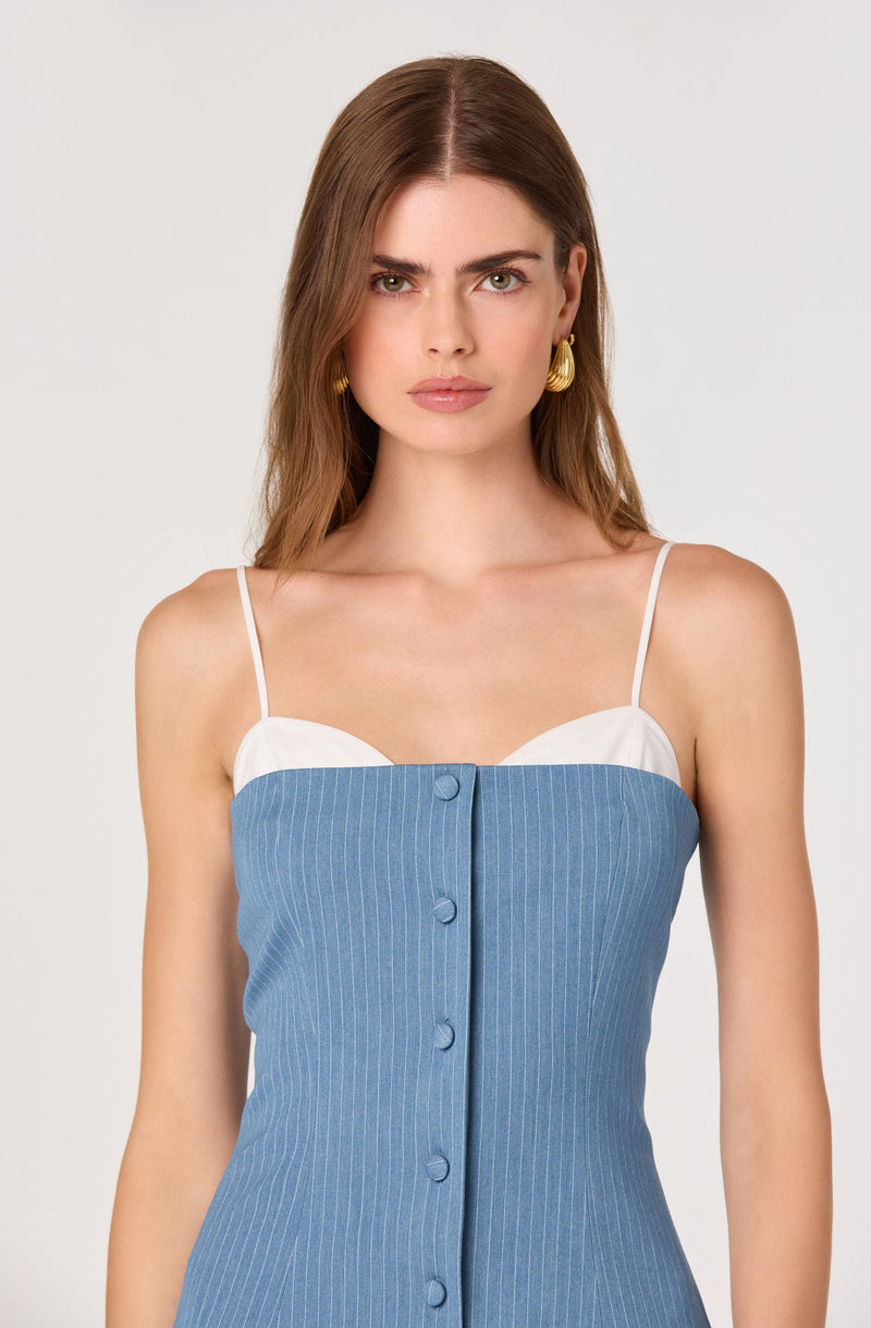 Woman in a blue pinstriped dress with white trim, thin white straps, and gold earrings.
