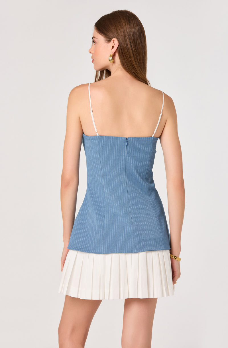 Woman in a blue pinstriped sleeveless top with thin white straps, and a white pleated skirt.