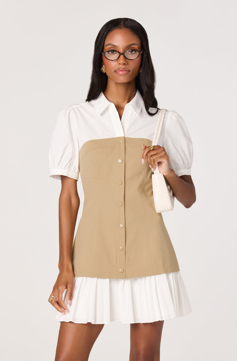 Woman in white blouse with puffed sleeves and beige button-down dress, holding a white handbag.