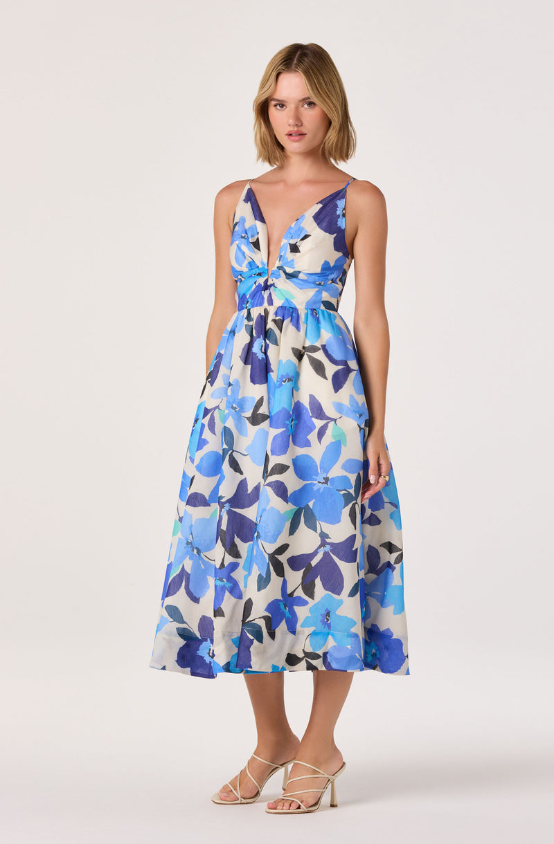 Woman wearing a sleeveless, V-neck, floral print dress with blue, white, and purple colors, and beige high-heeled sandals.