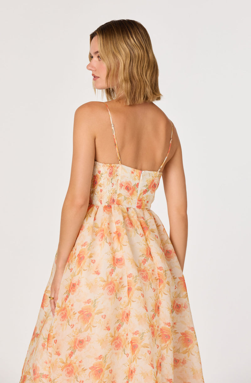 Woman in a floral sleeveless dress with thin straps and a fitted waist, flowing skirt.