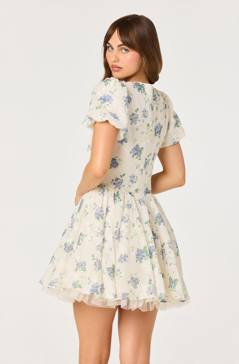 Girl in a cream dress with blue floral print and puffed short sleeves.