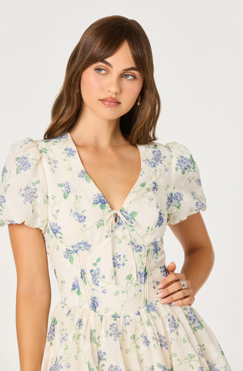 Cream dress with blue and green floral print, puffed short sleeves, and a tie at the neckline.