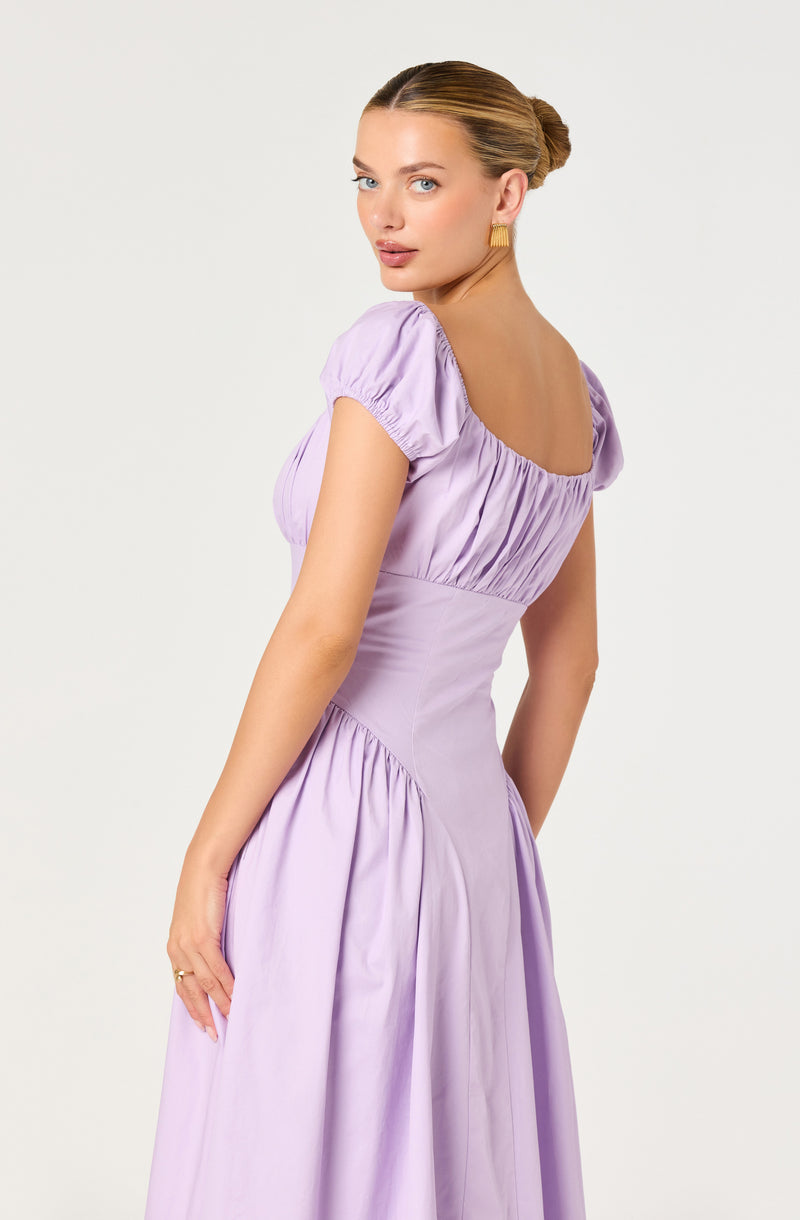 Woman in a lavender dress with puffed sleeves and a gathered waist, standing against a white background.