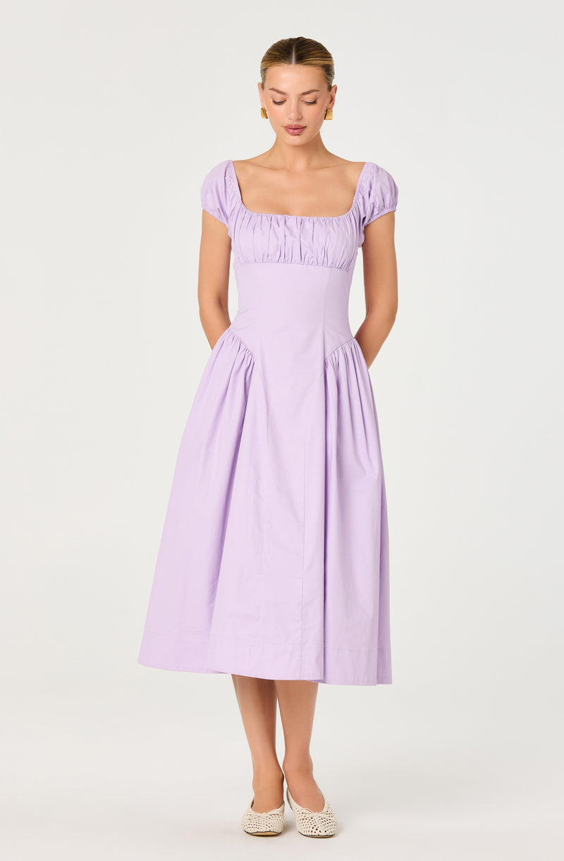 Woman in a light purple dress with puffed short sleeves, fitted waist, and full skirt.