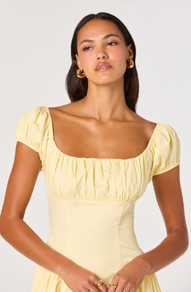 Woman in a yellow dress with ruched puff sleeves and a square neckline.