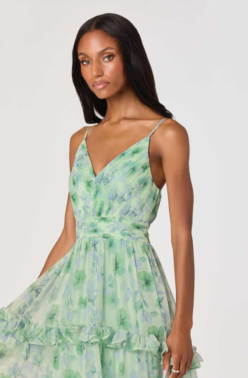 Woman wearing a light green, floral-printed, flowy dress with thin spaghetti straps.