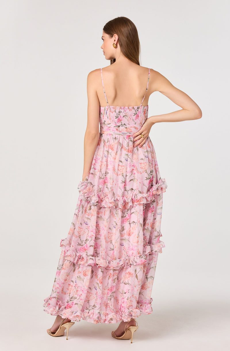 Woman wearing a long, pink floral dress with ruffled layers and thin spaghetti straps.