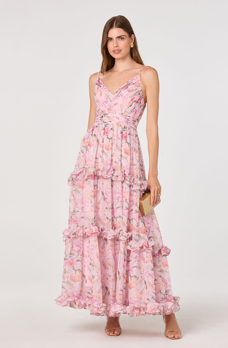 Woman in a long, pink floral dress with ruffled tiers and thin straps, holding a small clutch.