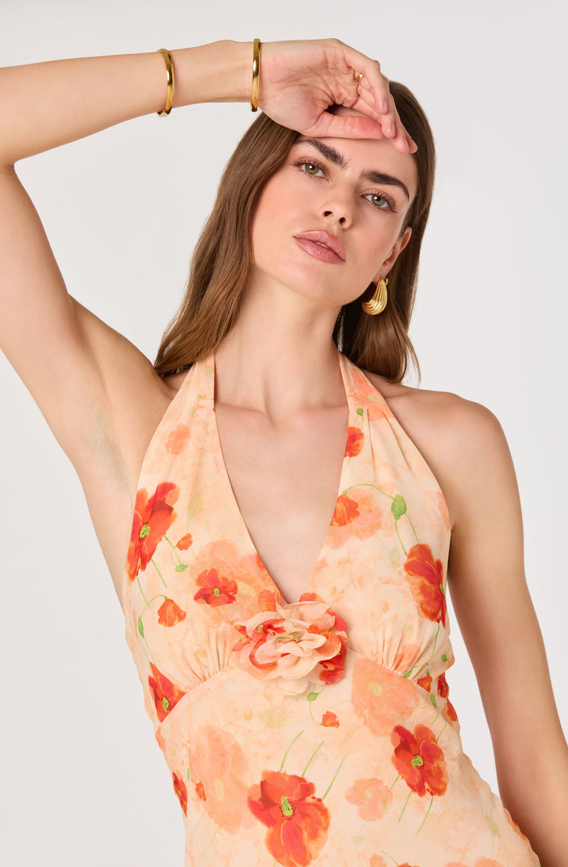Woman wearing a peach-colored dress with red and orange floral pattern, halter neck style.