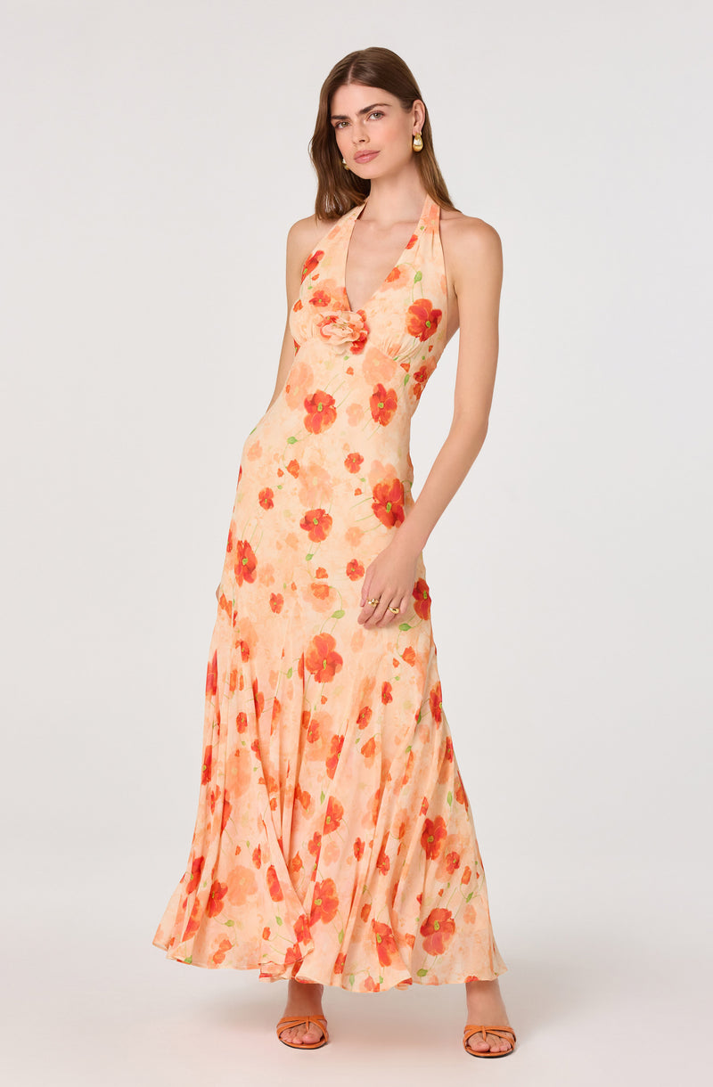 Woman wearing a sleeveless, peach-colored maxi dress with red and orange floral print.