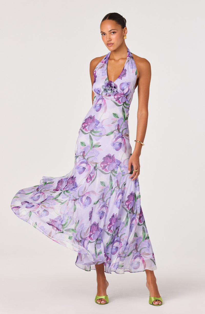 Woman wearing a sleeveless, halter-neck dress with a purple and green floral pattern.
