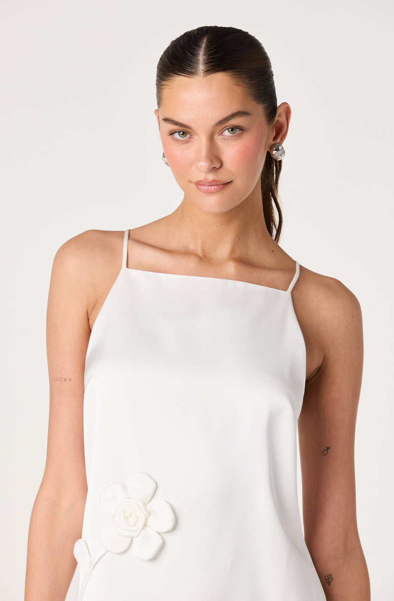Woman in a white spaghetti strap dress with floral embroidery on the lower side.