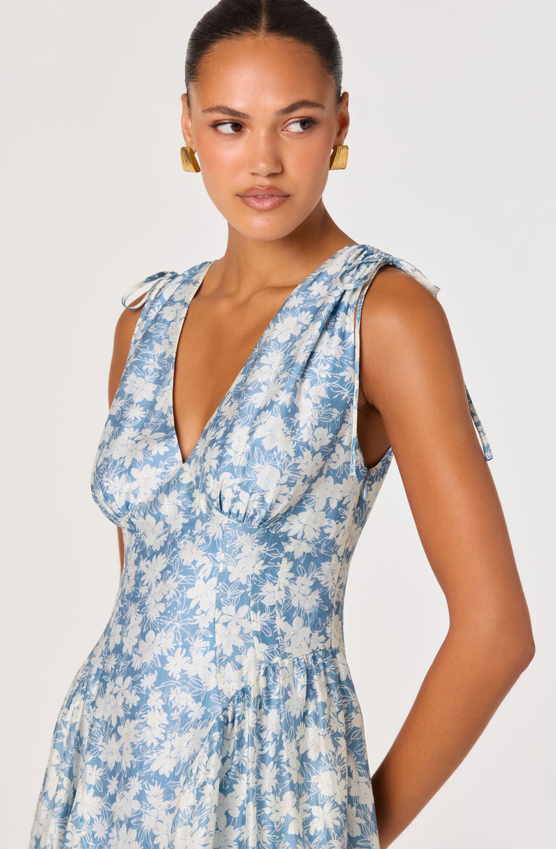 Woman wearing a sleeveless, blue and white floral dress with shoulder ties.