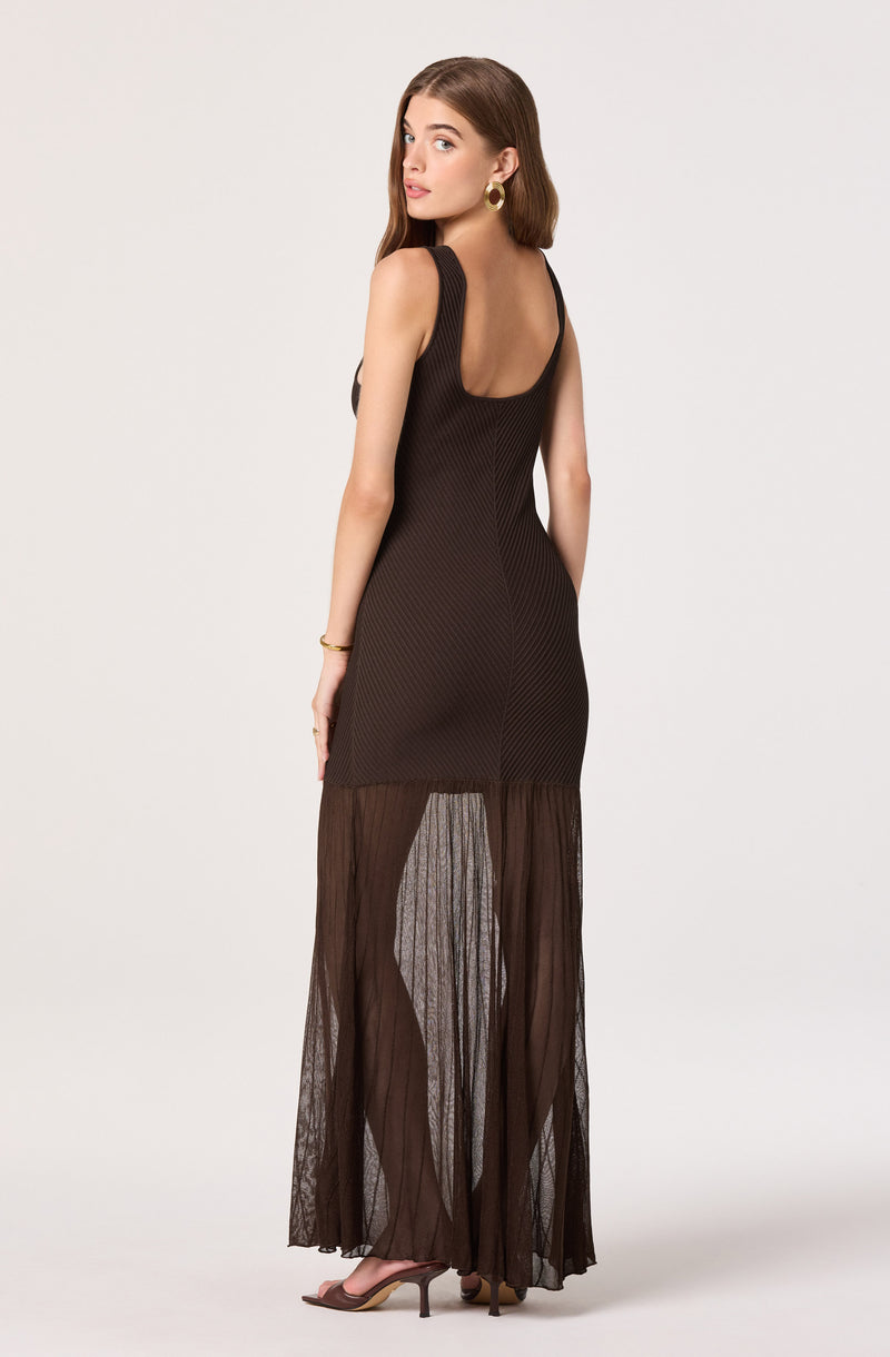 Model wearing a sleeveless black dress with a fitted bodice and sheer, pleated, wide-leg pants.