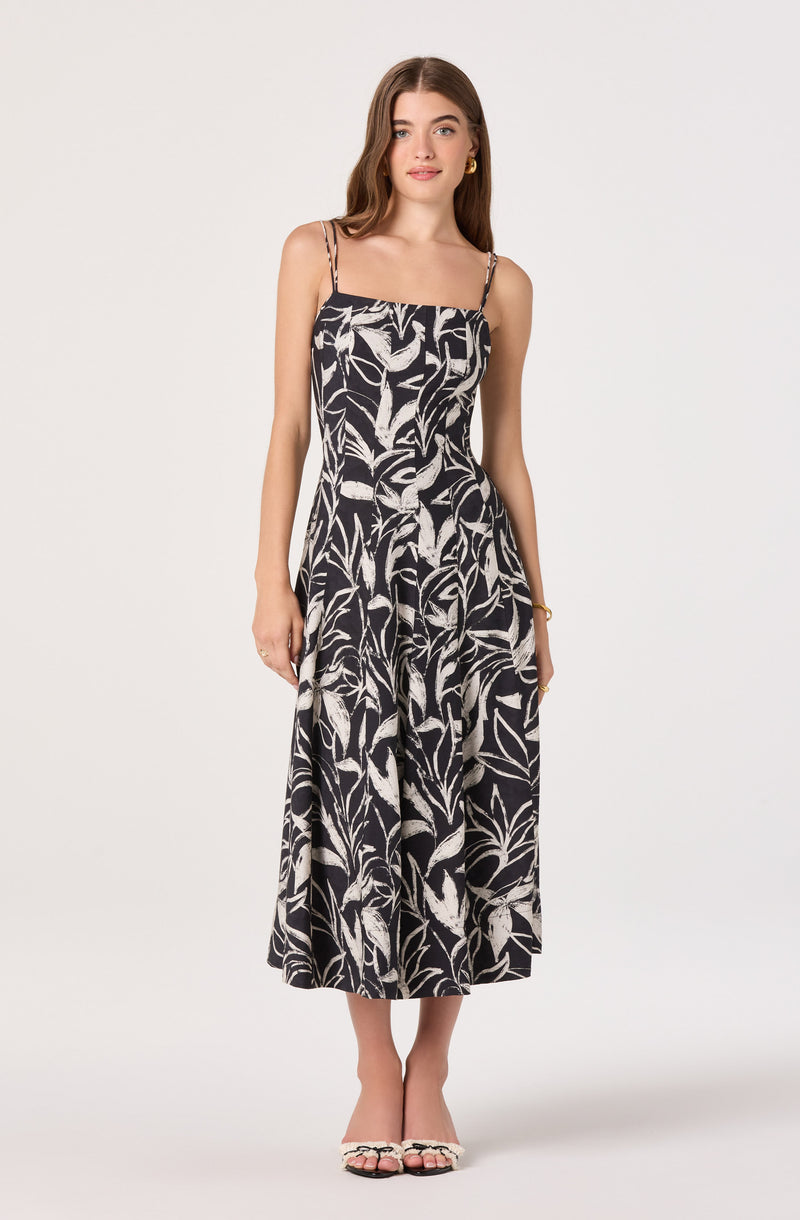 Woman in a black and white floral pattern sleeveless dress with spaghetti straps.