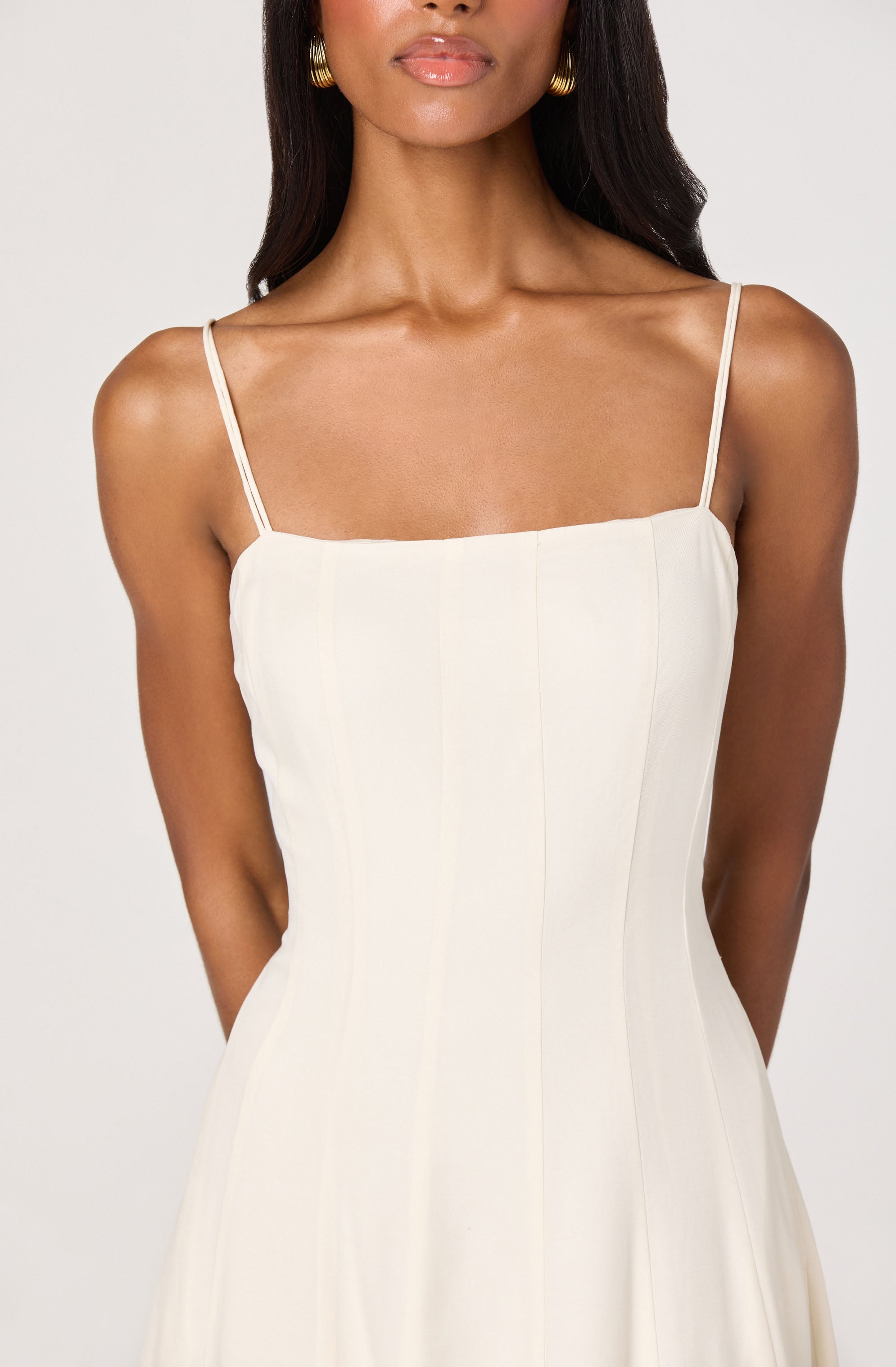 Woman wearing a white, sleeveless dress with thin spaghetti straps.