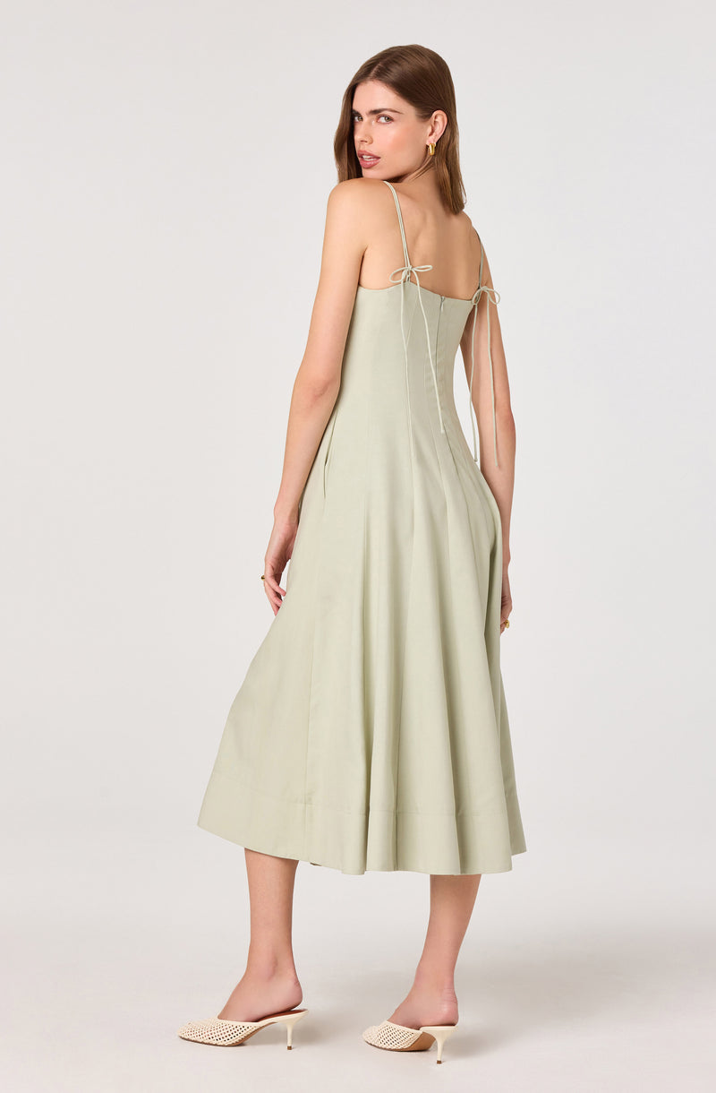 Woman in a light beige, sleeveless, spaghetti strap dress with tied straps, paired with cream-colored heels.