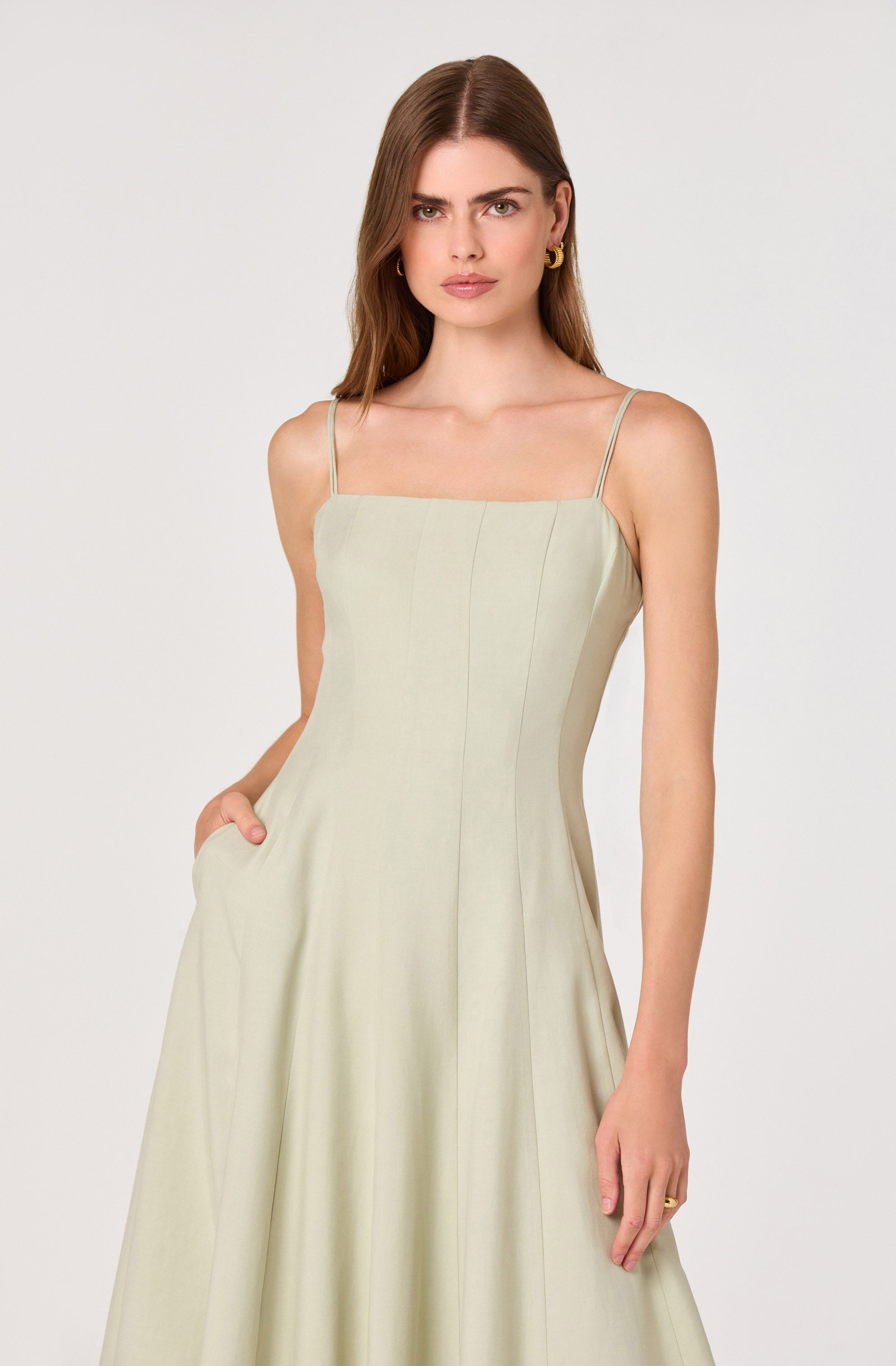 Woman in a light beige sleeveless dress with thin spaghetti straps and a pleated skirt.