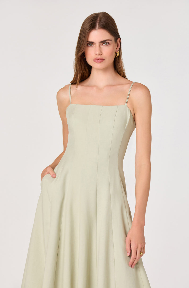 Woman in a light beige sleeveless dress with thin spaghetti straps and a pleated skirt.