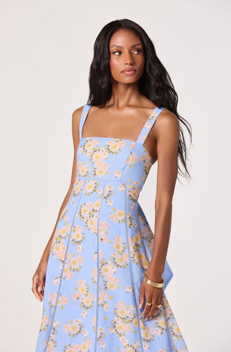 Woman in a light blue floral dress with thick shoulder straps and a fitted bodice, flowing skirt.