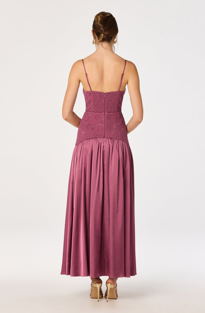 Back view of a woman in a long, pleated satin dress with a fitted lace bodice and thin spaghetti straps.