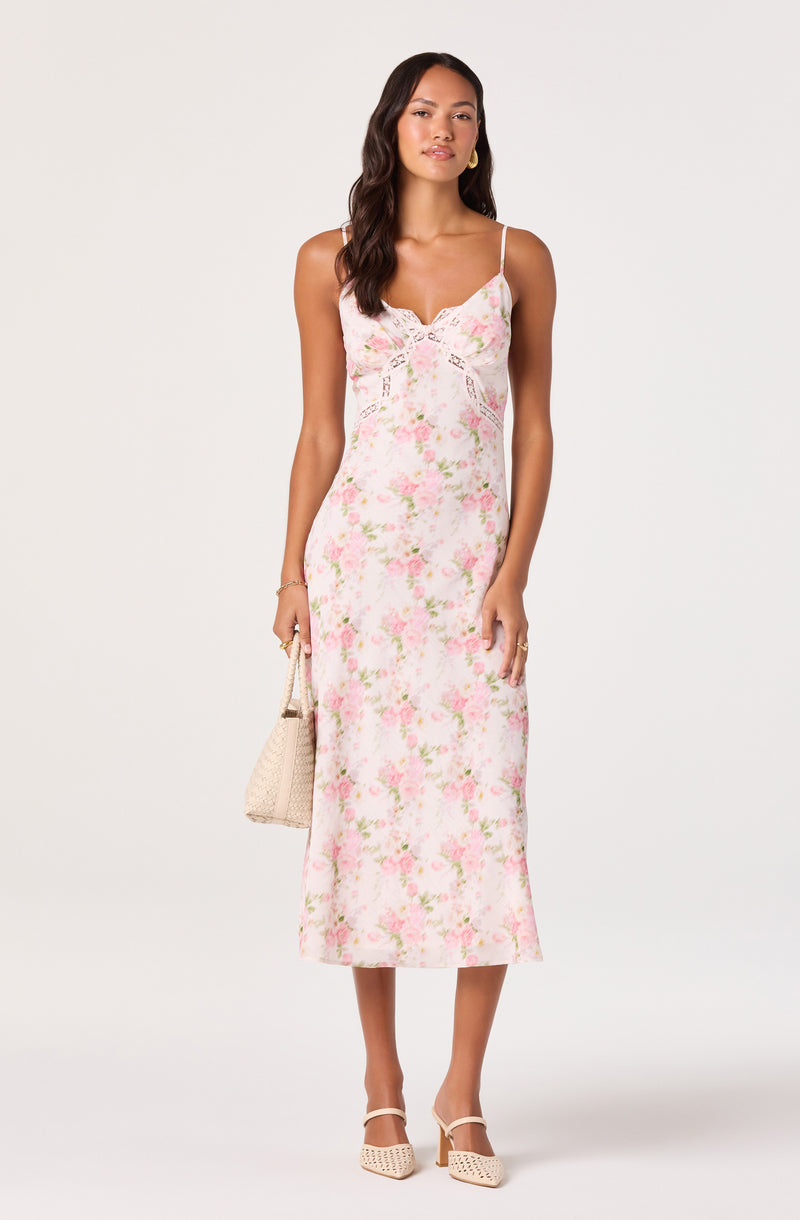Woman in a pink floral slip dress with spaghetti straps, carrying a beige woven bag.