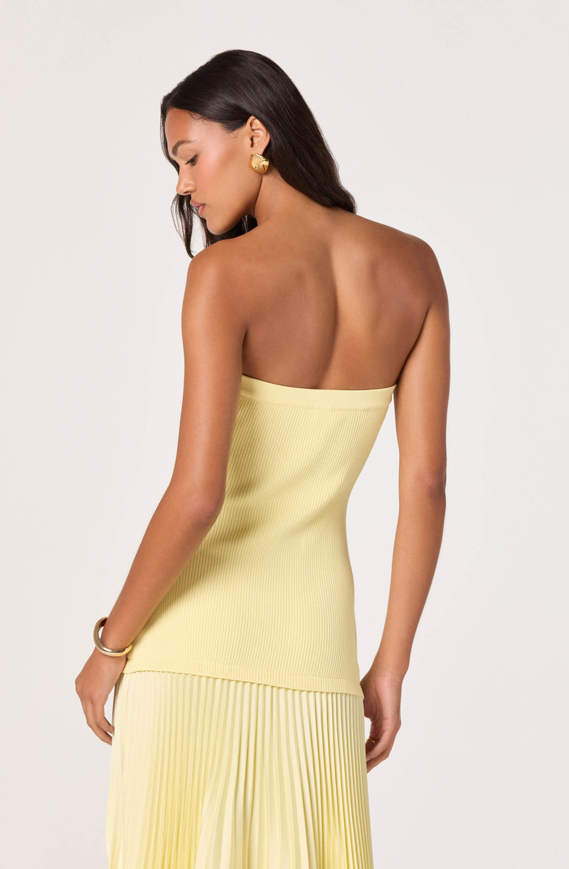 Woman in a strapless, pale yellow ribbed top and matching pleated skirt.