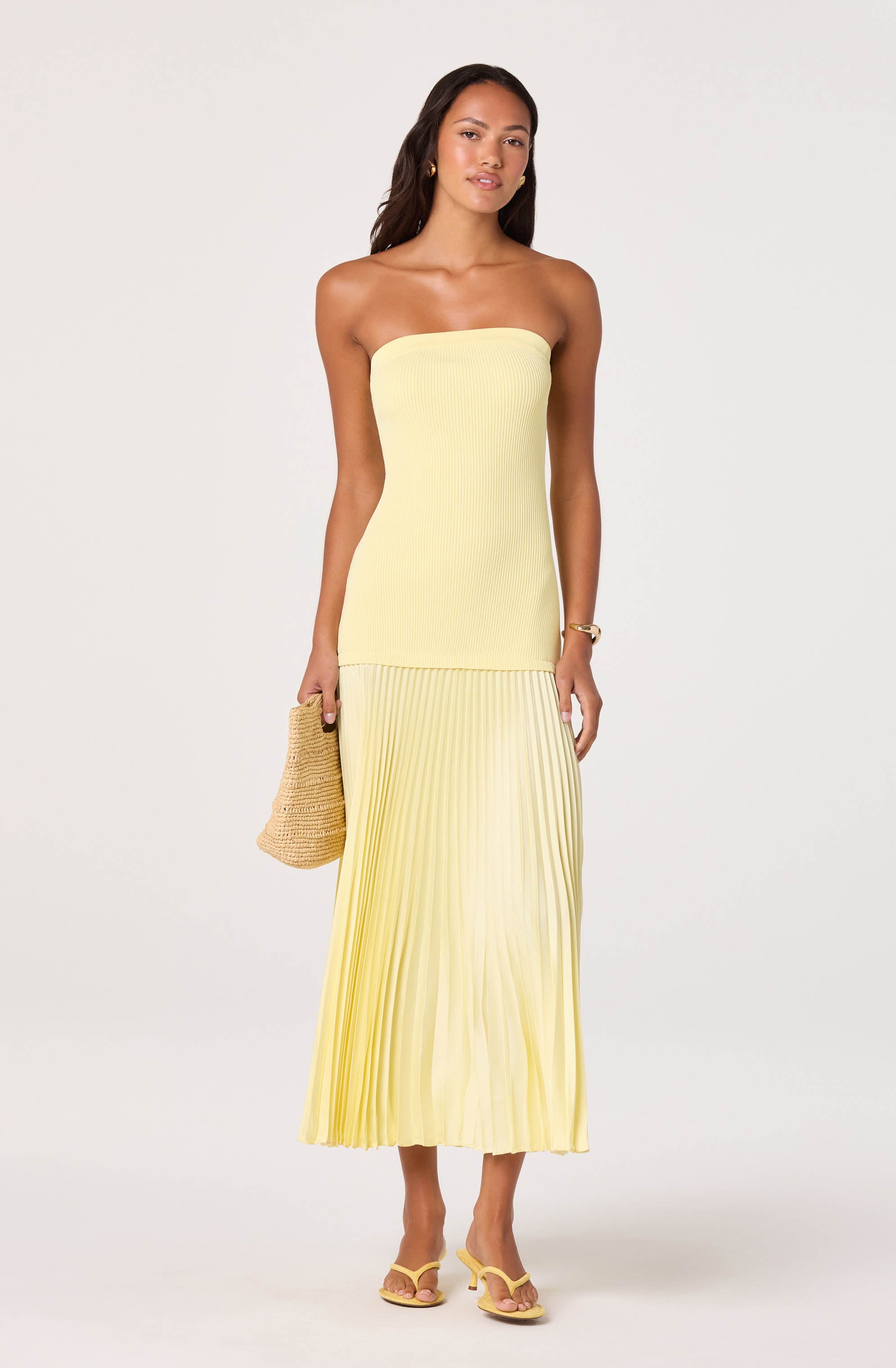 Light yellow strapless dress with a fitted top and pleated skirt, paired with yellow heels and a woven bag.