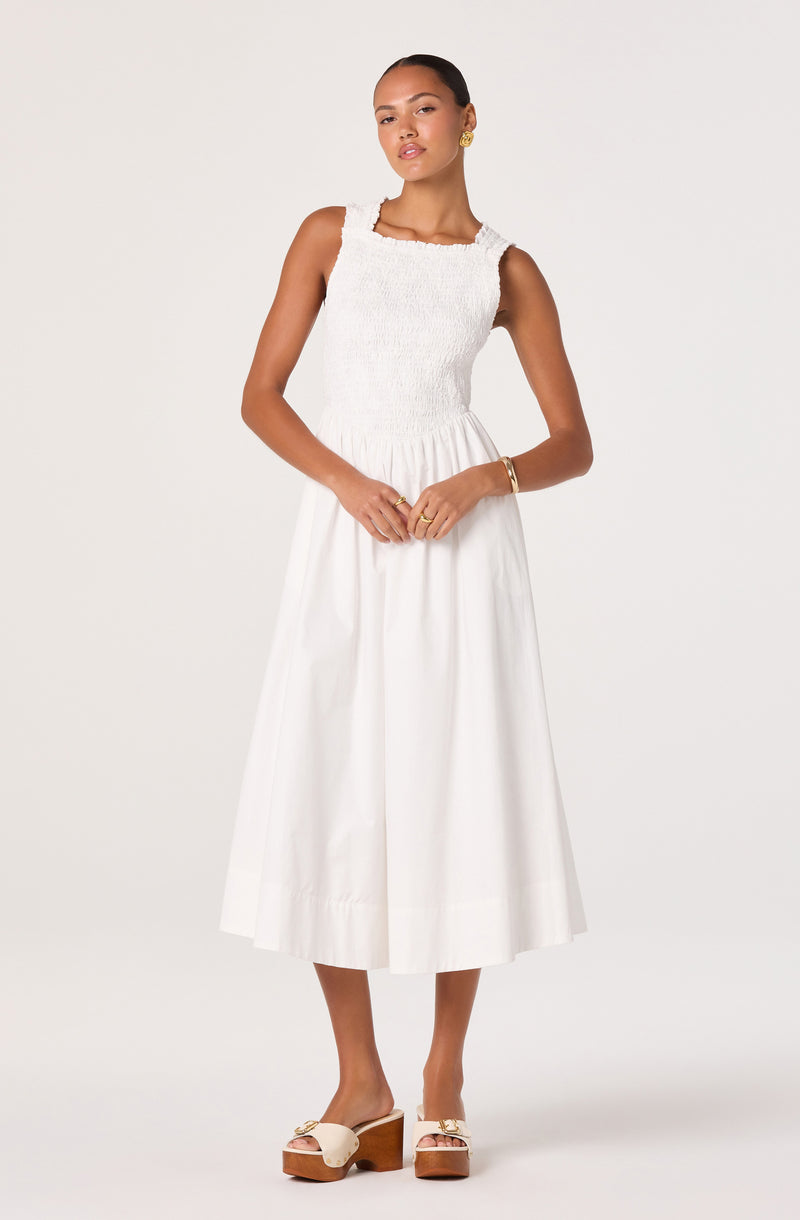Woman wearing a sleeveless white textured top and a long white skirt with platform sandals.