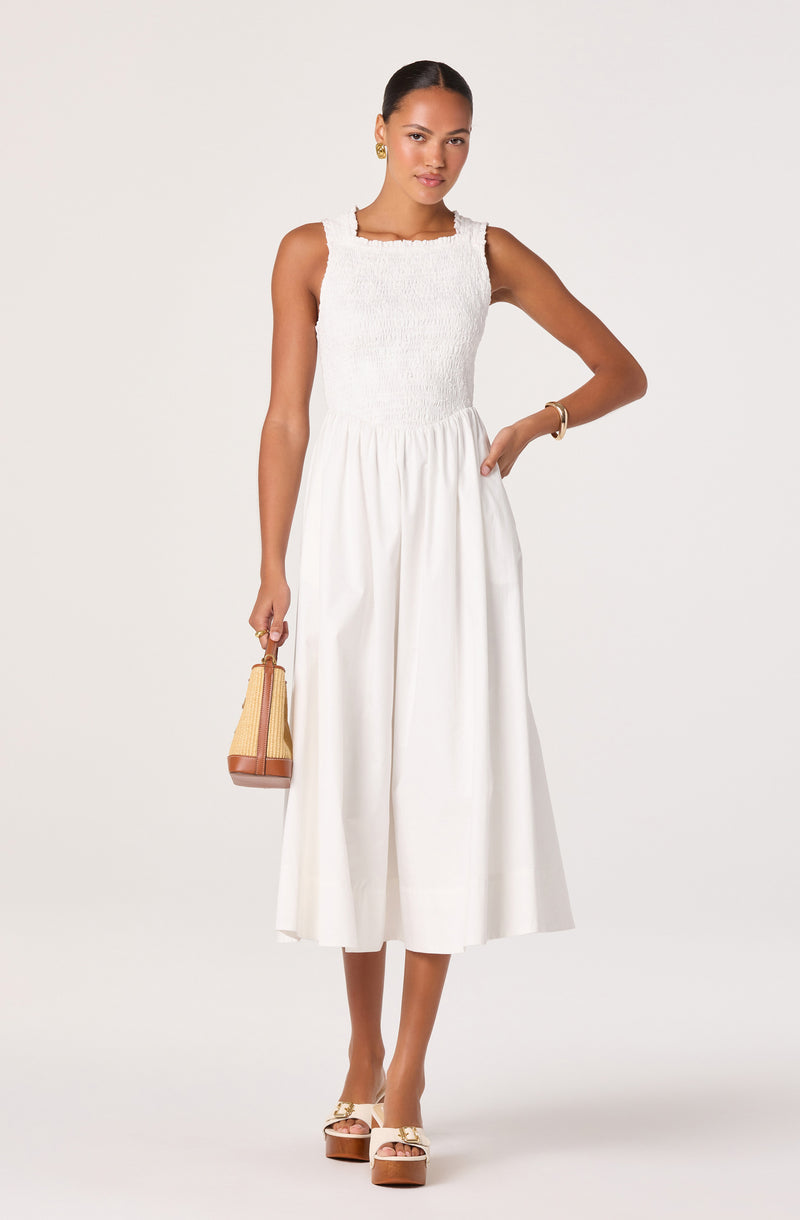 Woman in white sleeveless dress with textured bodice and wide-leg skirt, wearing gold jewelry.
