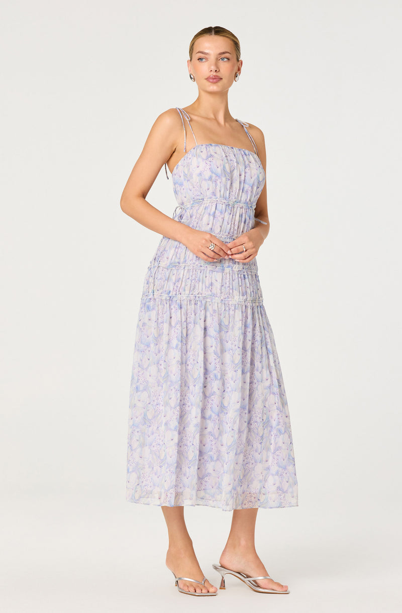 Woman wearing a pastel floral sleeveless dress with spaghetti straps and a tiered skirt.