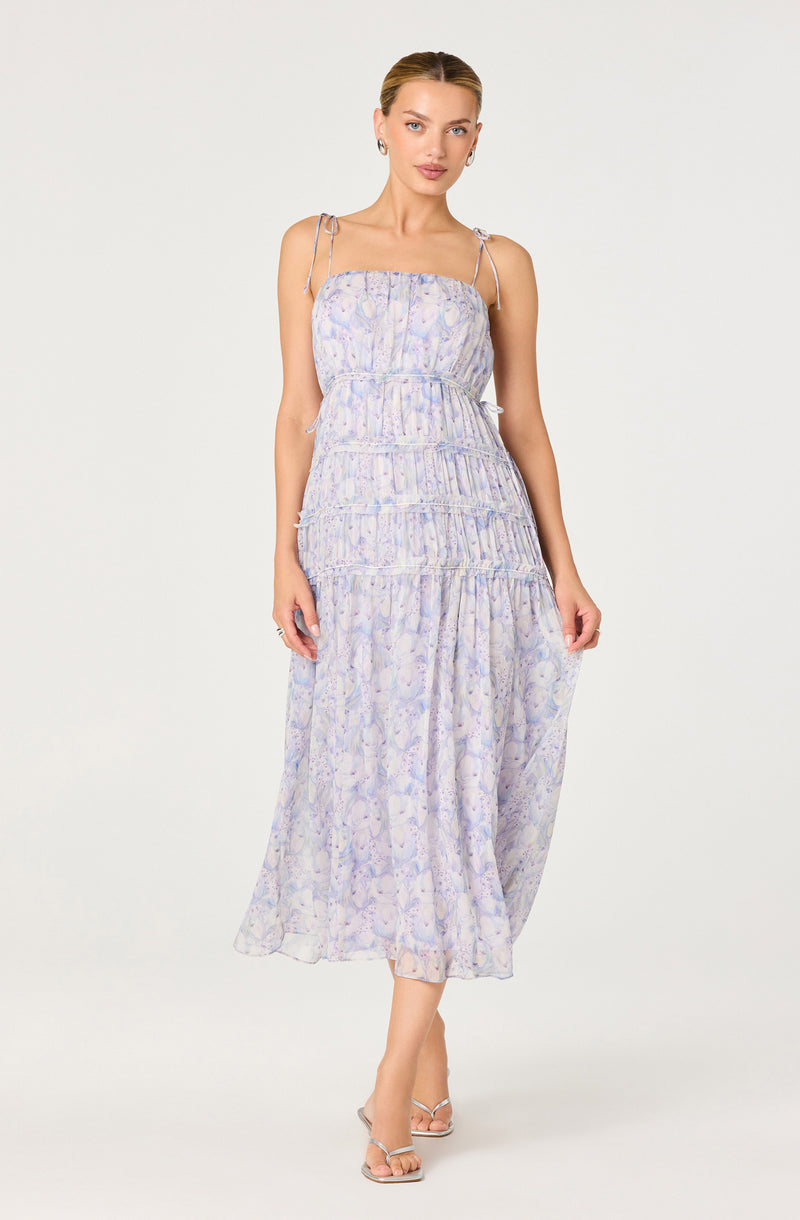 Woman in a light purple patterned summer dress with spaghetti straps and a flowy skirt.