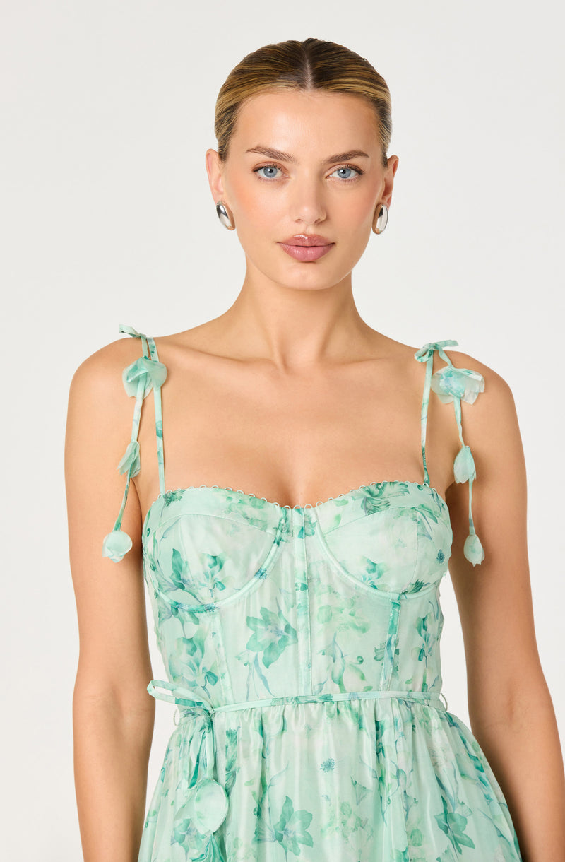 Woman wearing a light green floral dress with tied shoulder straps and a fitted bodice.