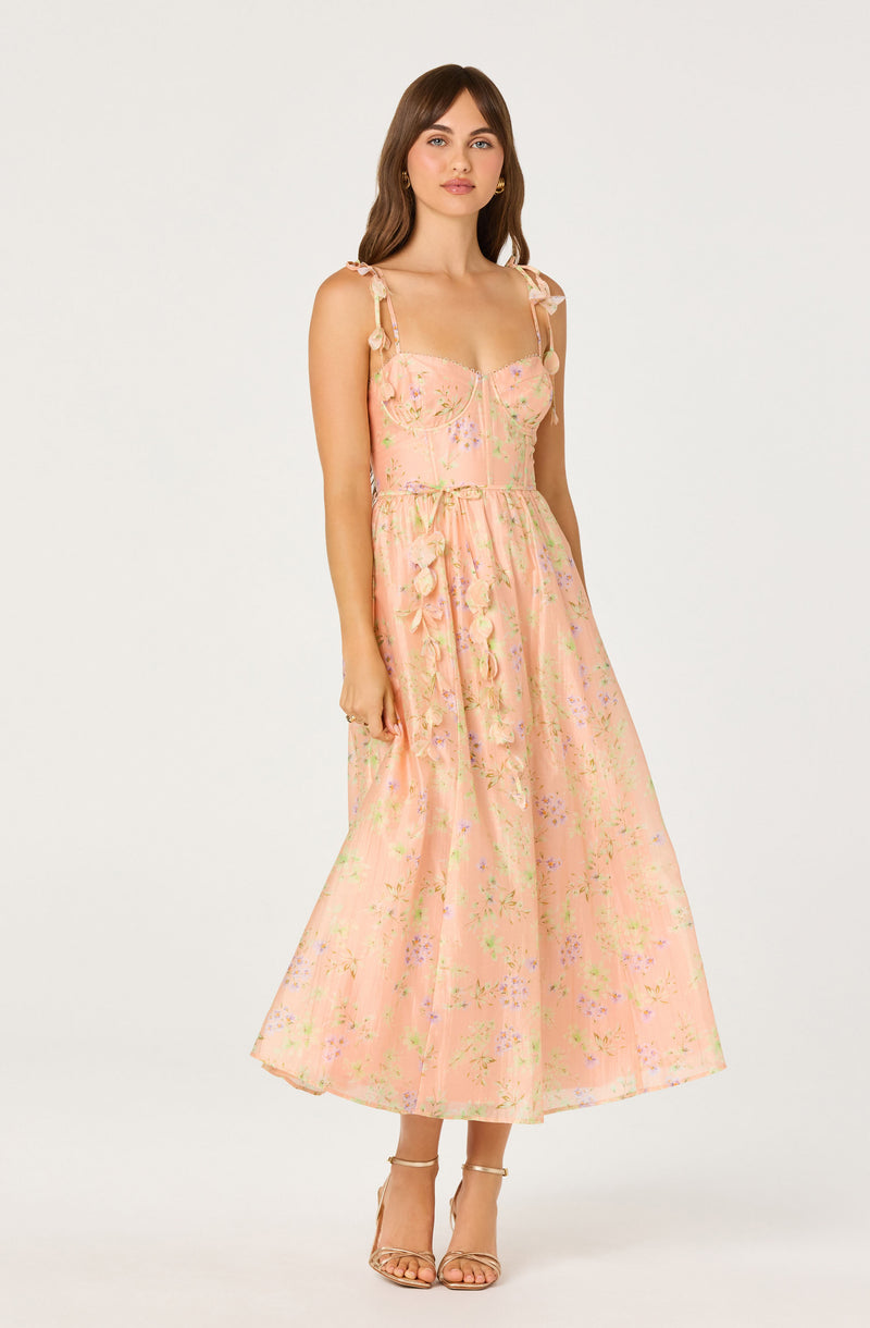 Woman in pink floral dress with bow straps and ruffled waist, wearing nude heels.