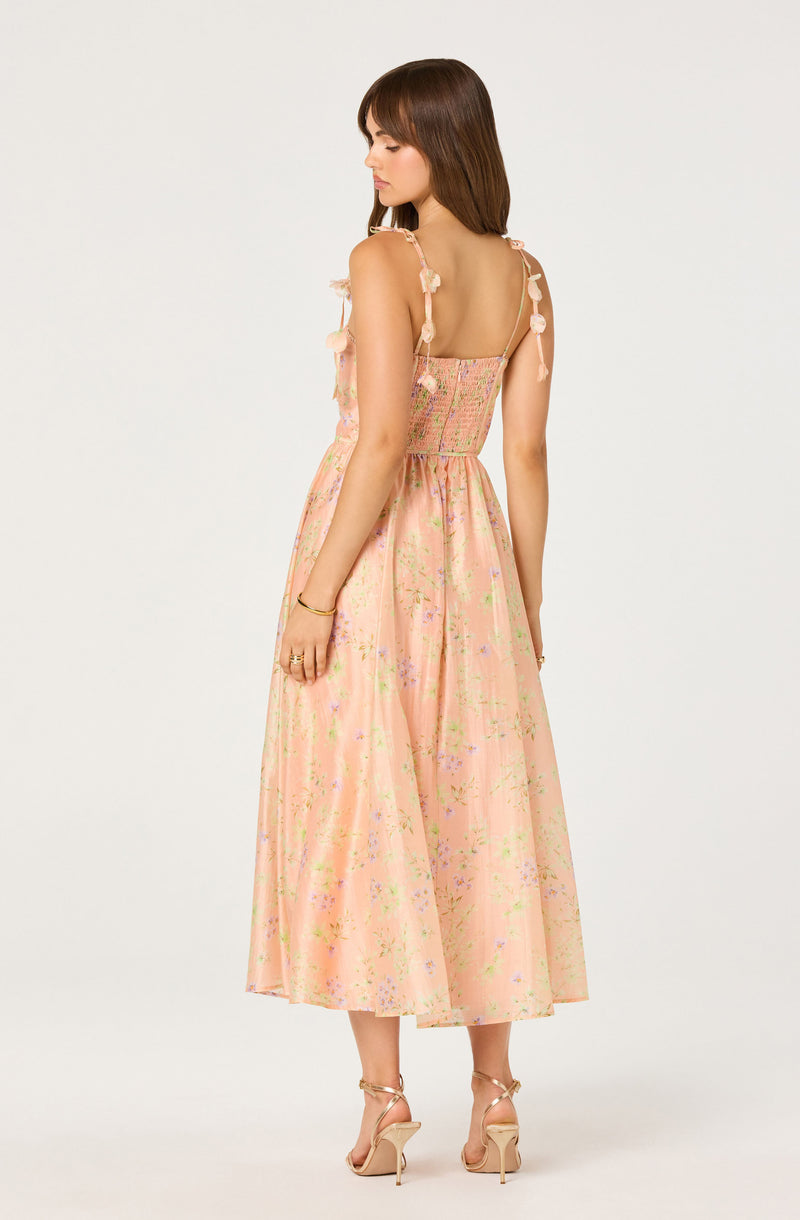 Girl wearing a peach floral maxi dress with bows on the straps and open back.
