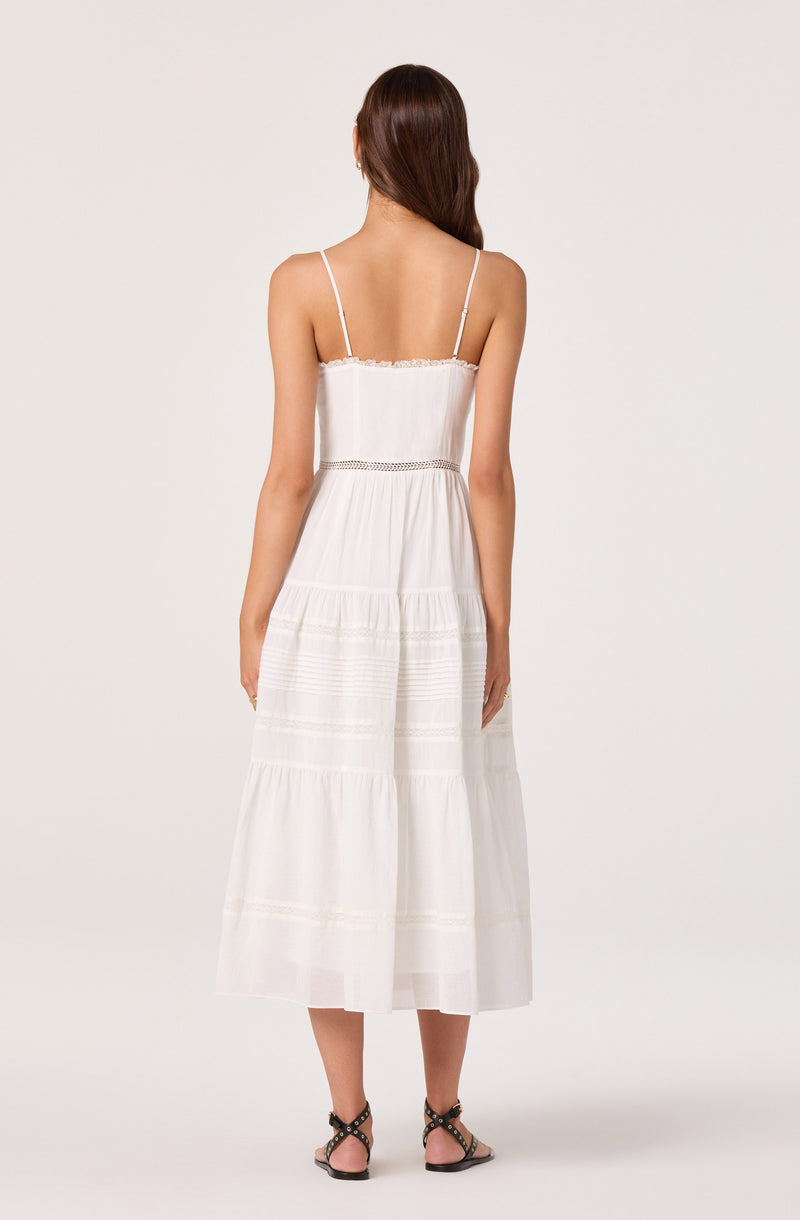 Woman in a long, white, sleeveless dress with spaghetti straps and a tiered skirt.