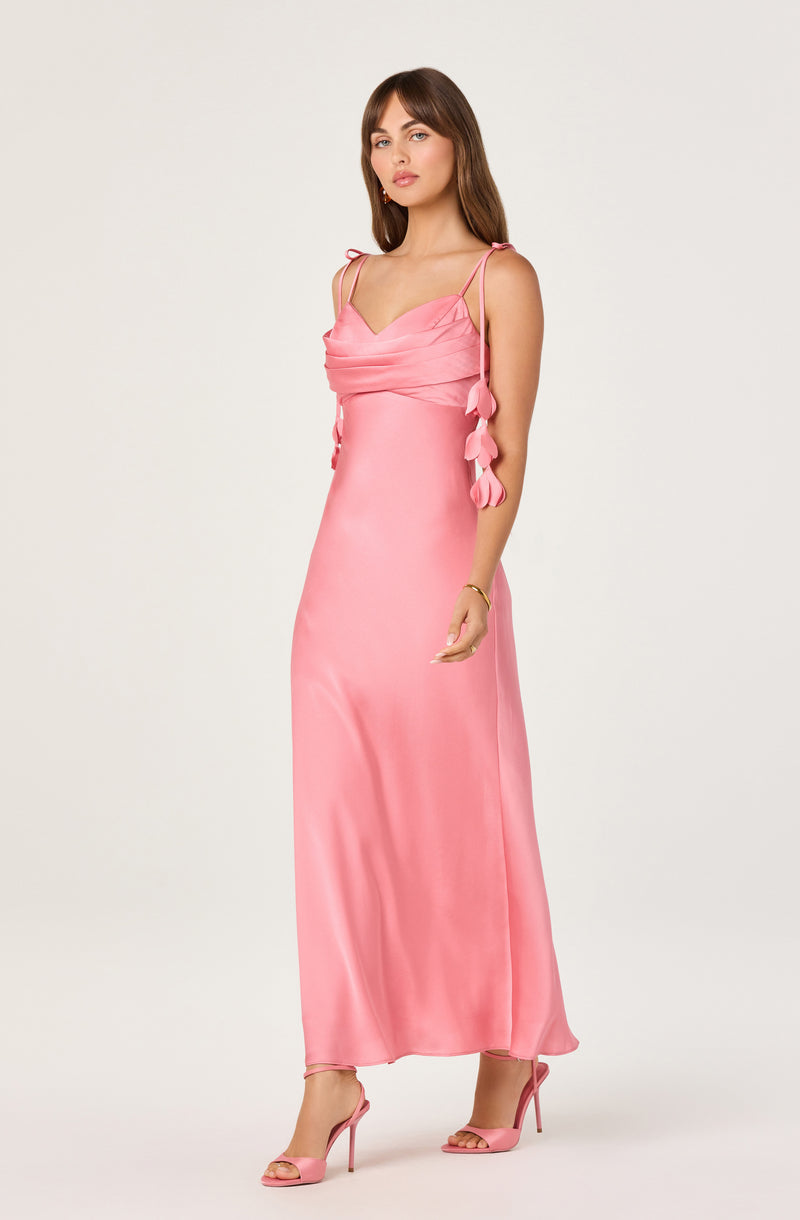 Woman in a long pink satin evening gown with spaghetti straps and decorative fabric flowers.
