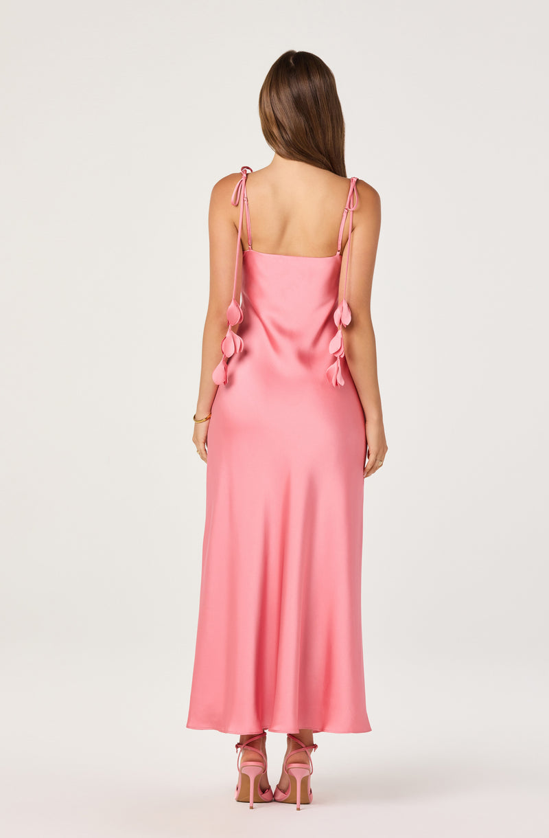 Woman in a long pink satin dress with tied straps featuring fabric bow details.